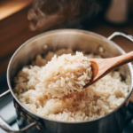 Overhead close-up of a pot of overcooked mushy white rice being stirred with a wooden spoon, steam rising softly